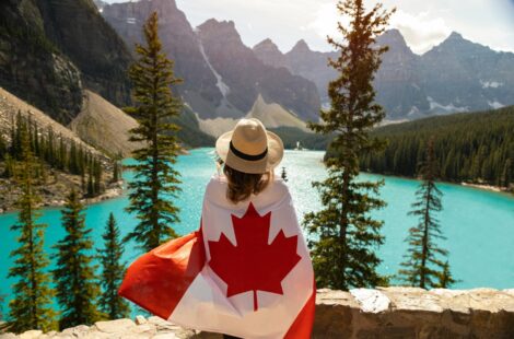 Une personne avec le drapeau du Canada regarde la vue de dos avec des montagnes et un lac